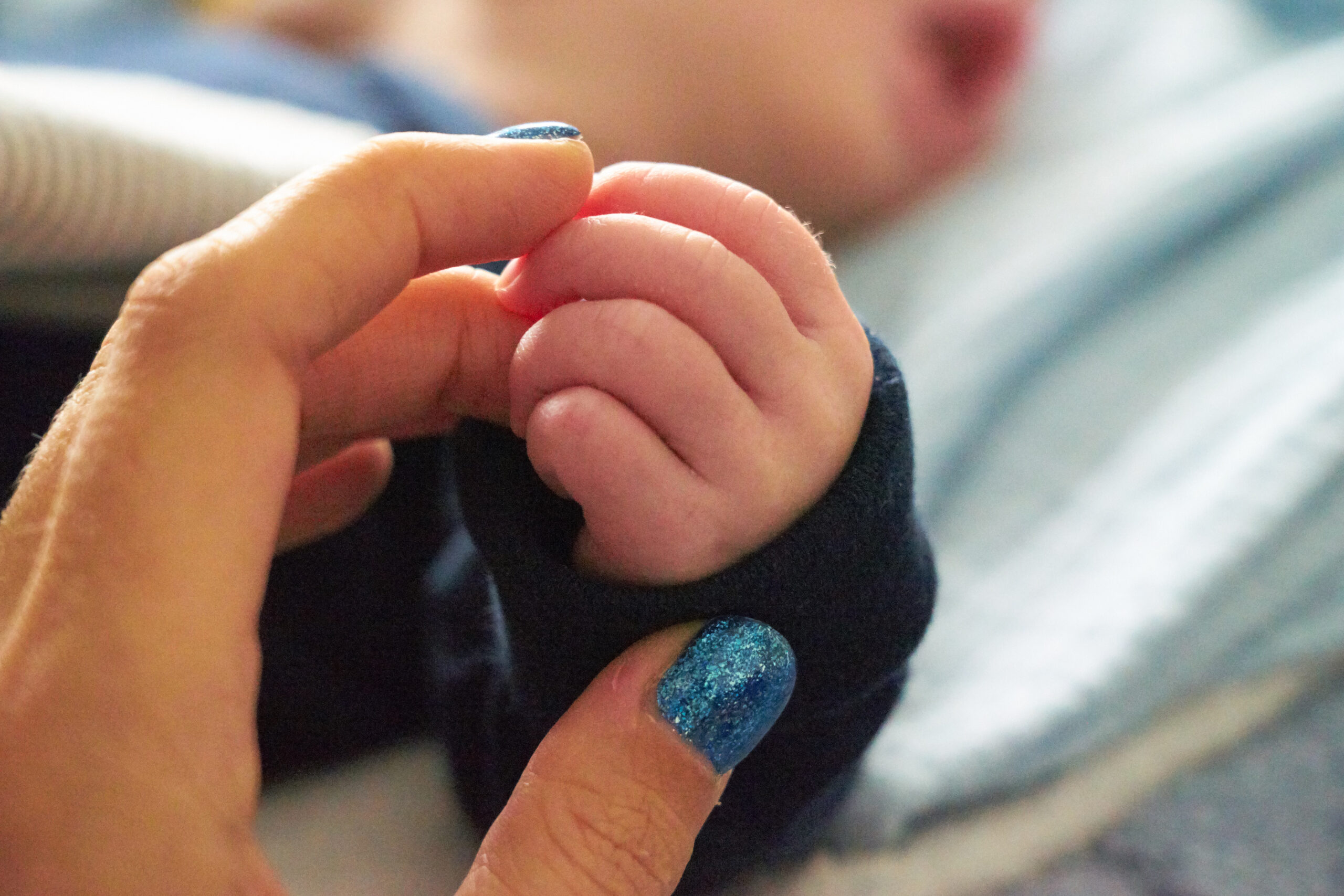 Detailaufnahme einer Hand, die die winzige Hand eines Babys zärtlich berührt. Symbolbild der Palliativpflege zu Hause.